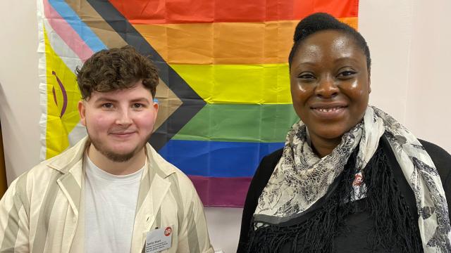 Jamie and Veronica stand in front of a pride flag
