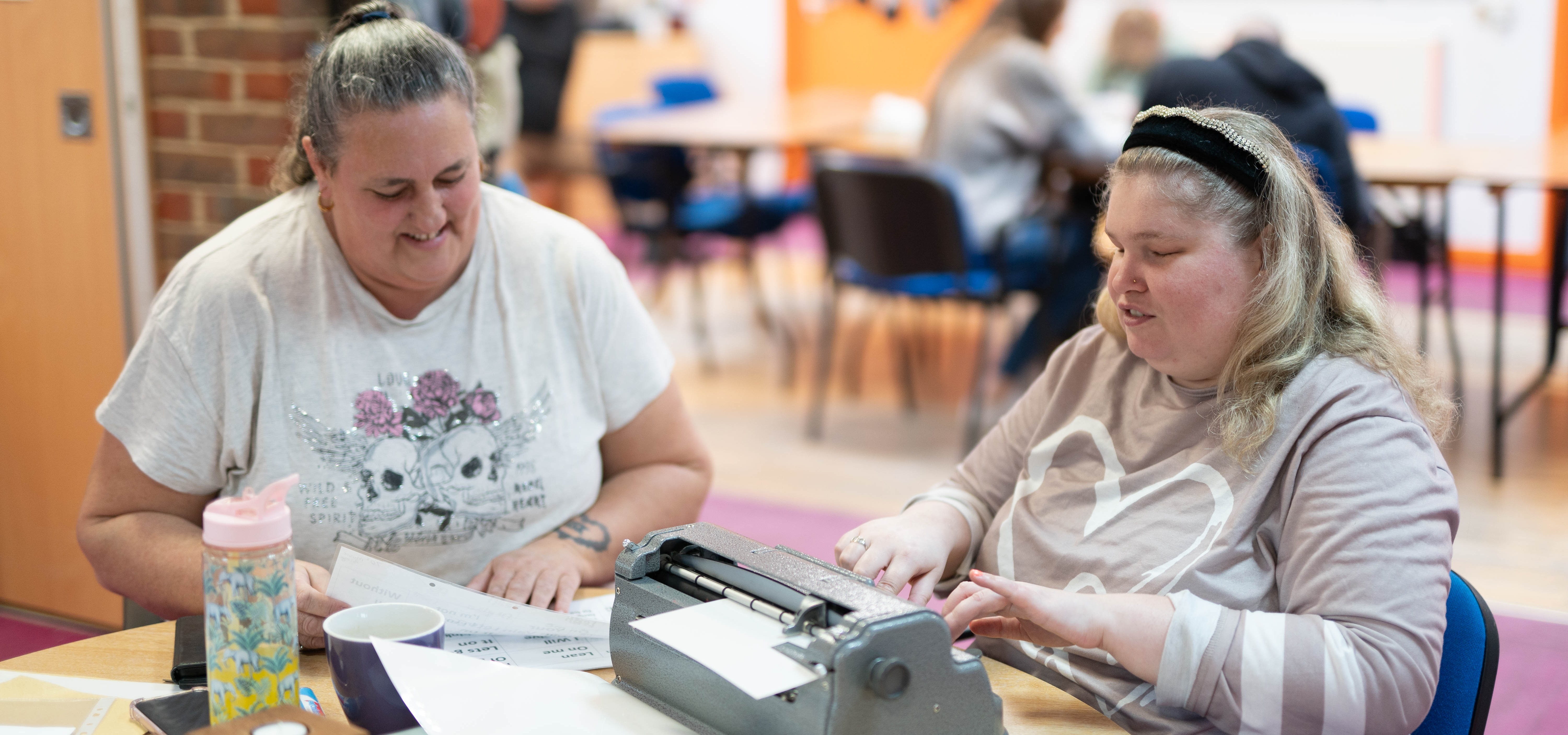 Joanne sitting next to a Support Worker and using a typewriter