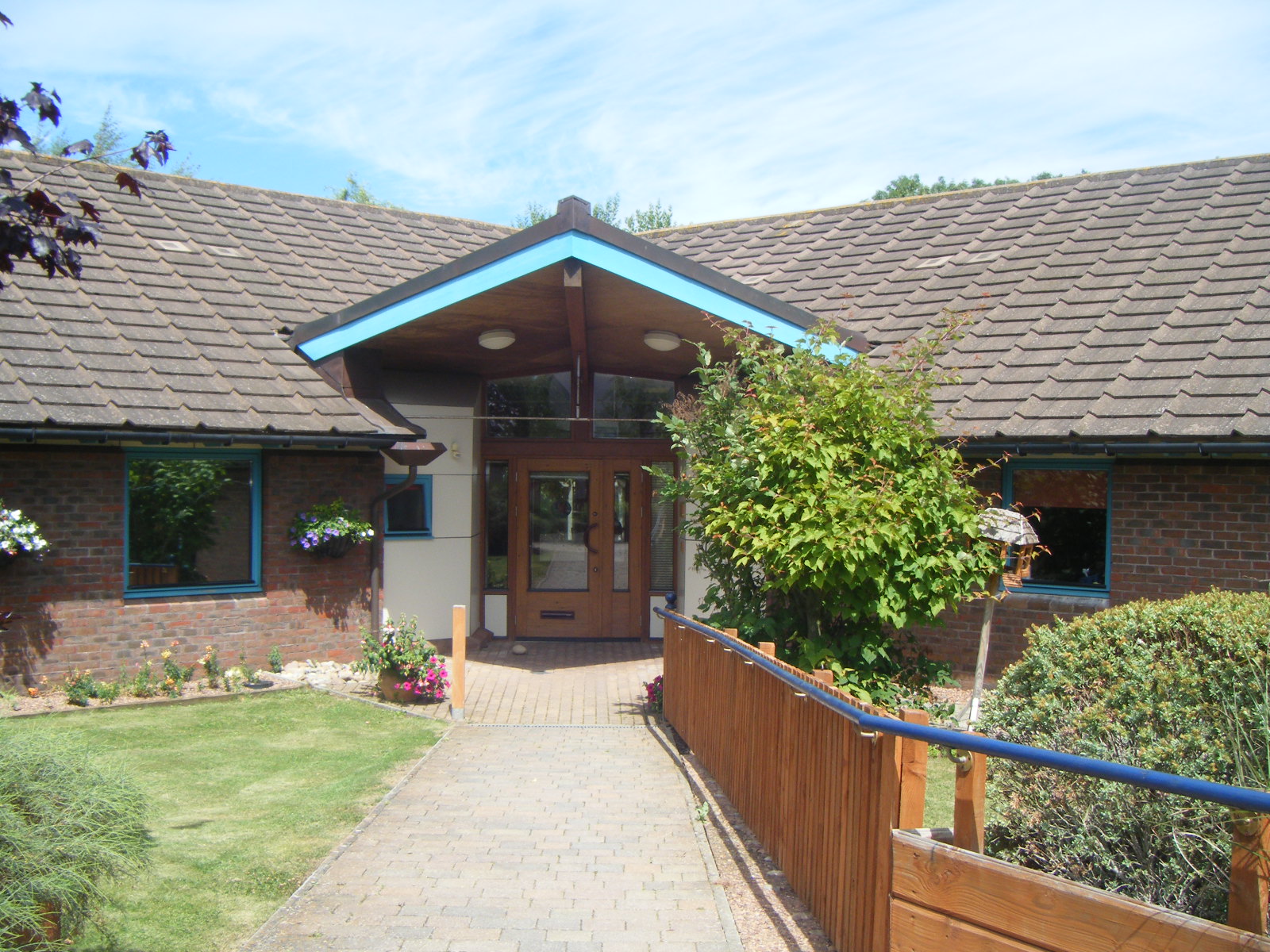 The outside of Fiennes House, showing a bright gabled entrance surrounded by flowers and greenery.
