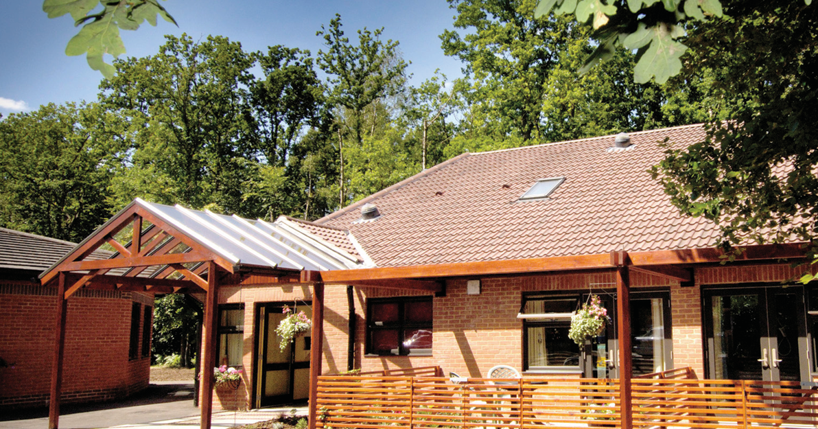 The outside of Fir Tree Lodge, showing a warm red-brick home tucked away in a lush woodland setting.