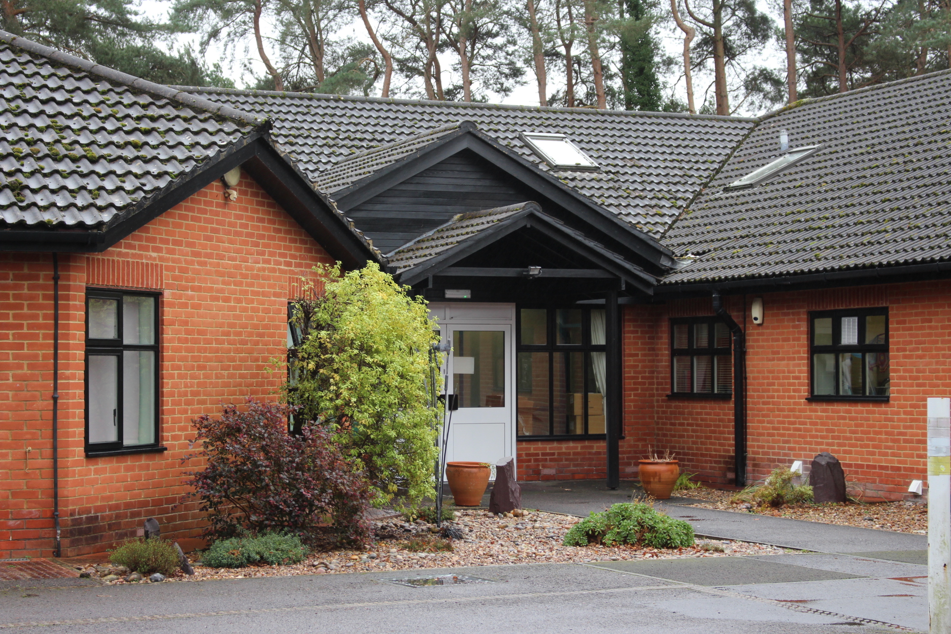 The outside of Heather House, a welcoming red-bricked home with a large gabled entrance, surrounded by a pebbled border and shrubbery.