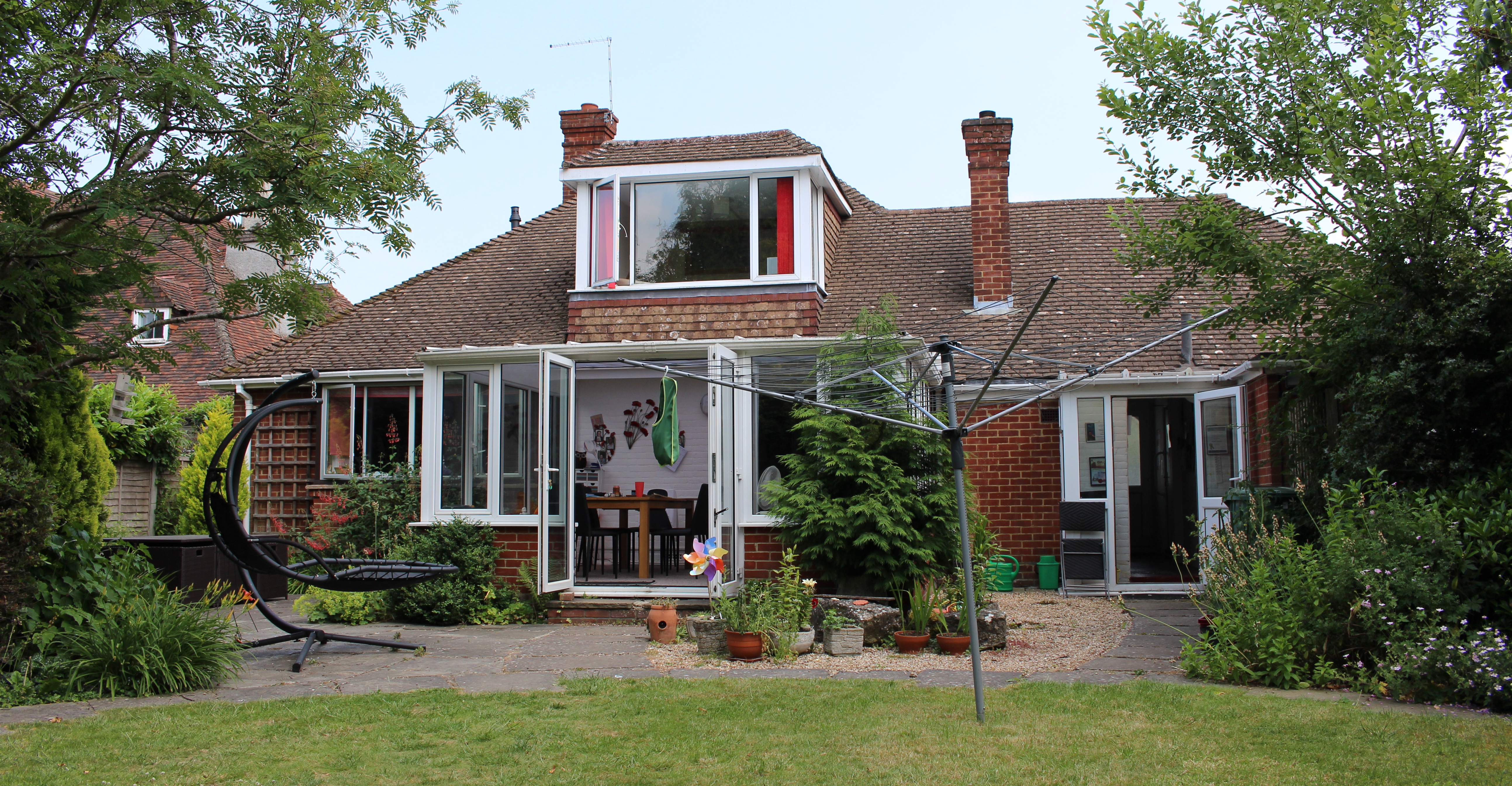 The back garden of a property in Maidstone, showing a spacious red-bricked property surrounded by greenery.