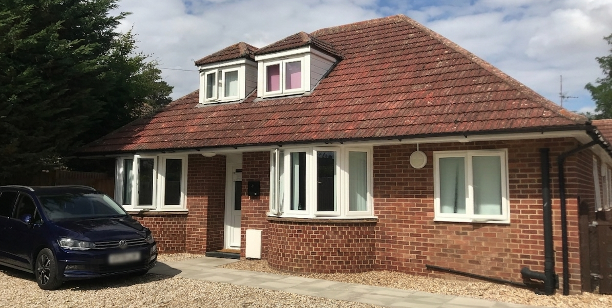 The outside of a red-brick bungalow in Oxfordshire, with bay windows and a pitched tiled roof.