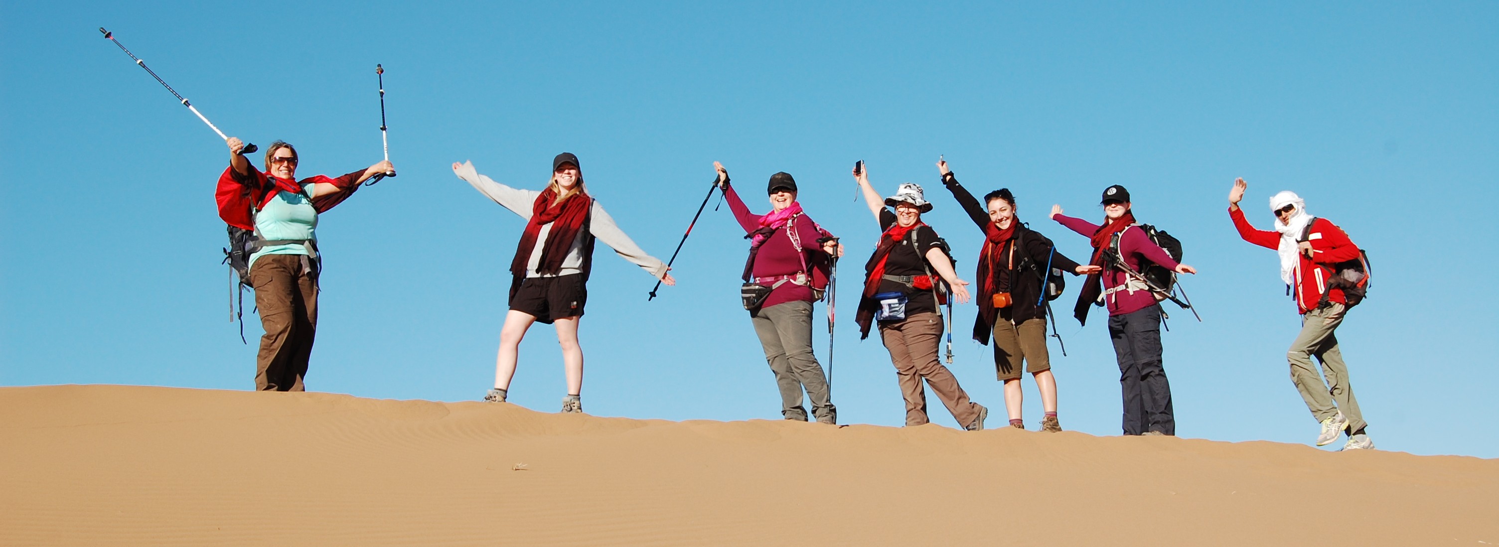 A group of adventurers smiling and waving at the Sahara Desert