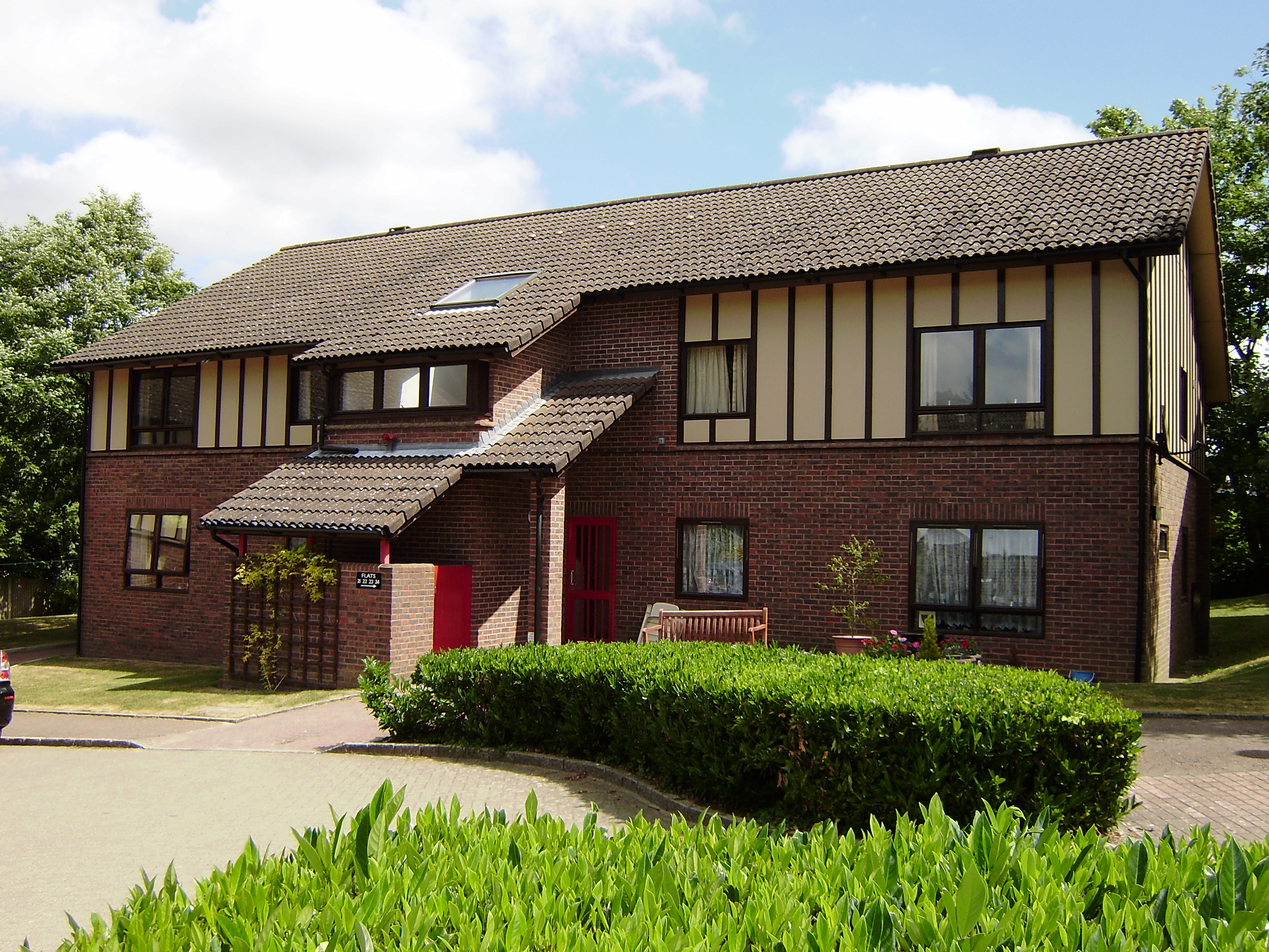 The outside of Spencer Court - a two-storey home with cream panelled upper walls, a pitched tiled roof and a small landscaped garden with bench seating.