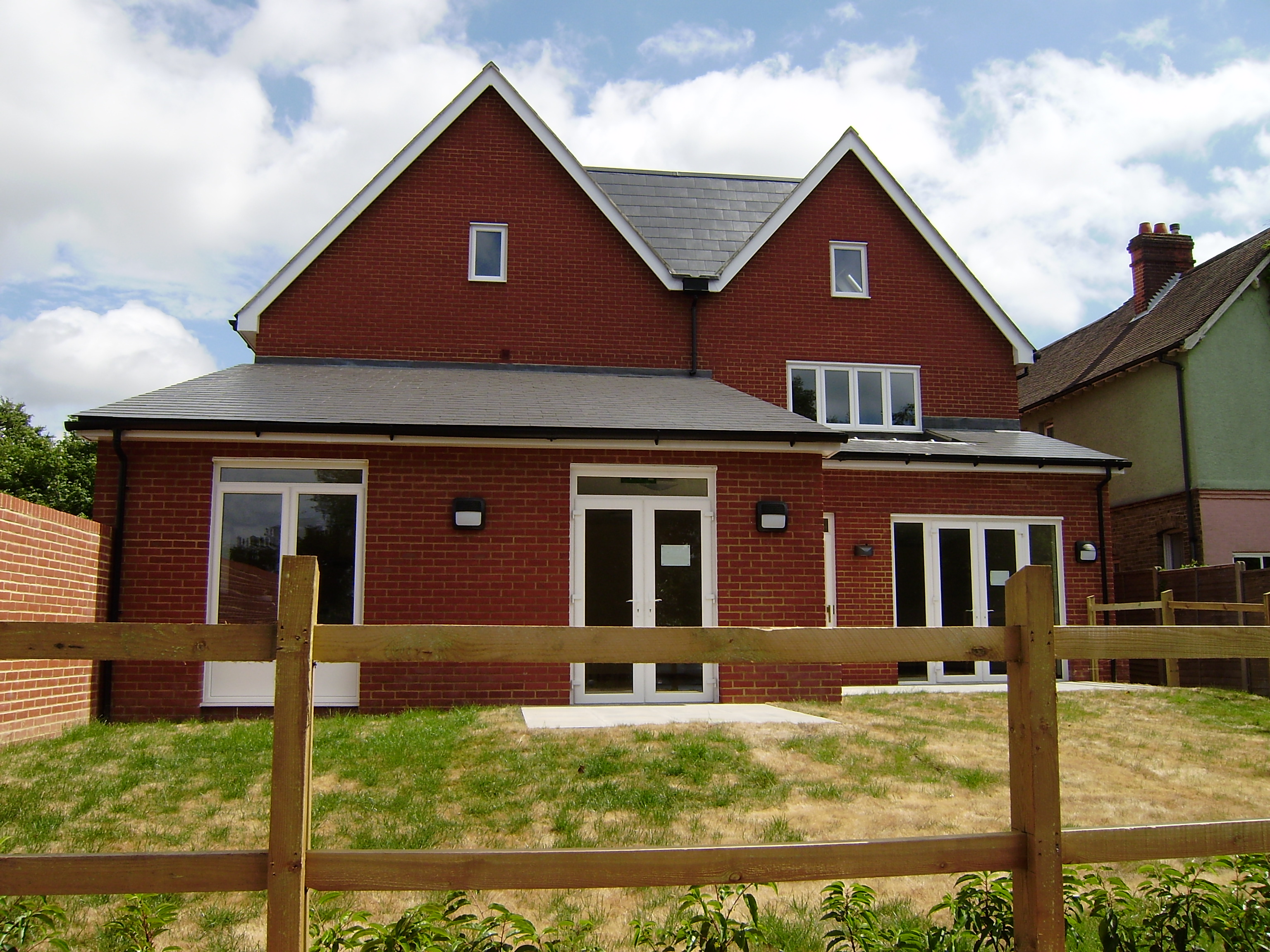 The outside of The Willows - a modern two-storey red brick building with pitched roofs, white-framed doors and windows, and garden space.