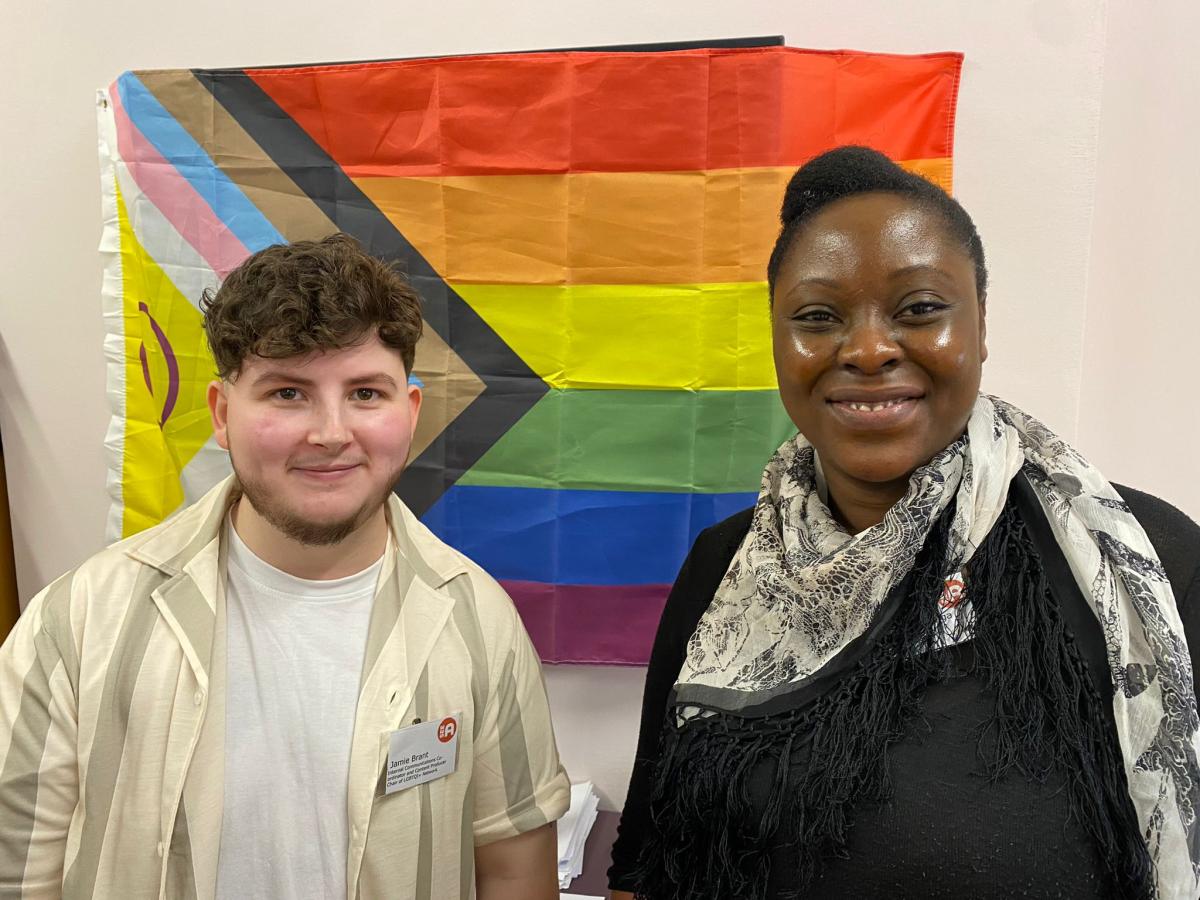 Jamie and Veronica stand in front of a pride flag