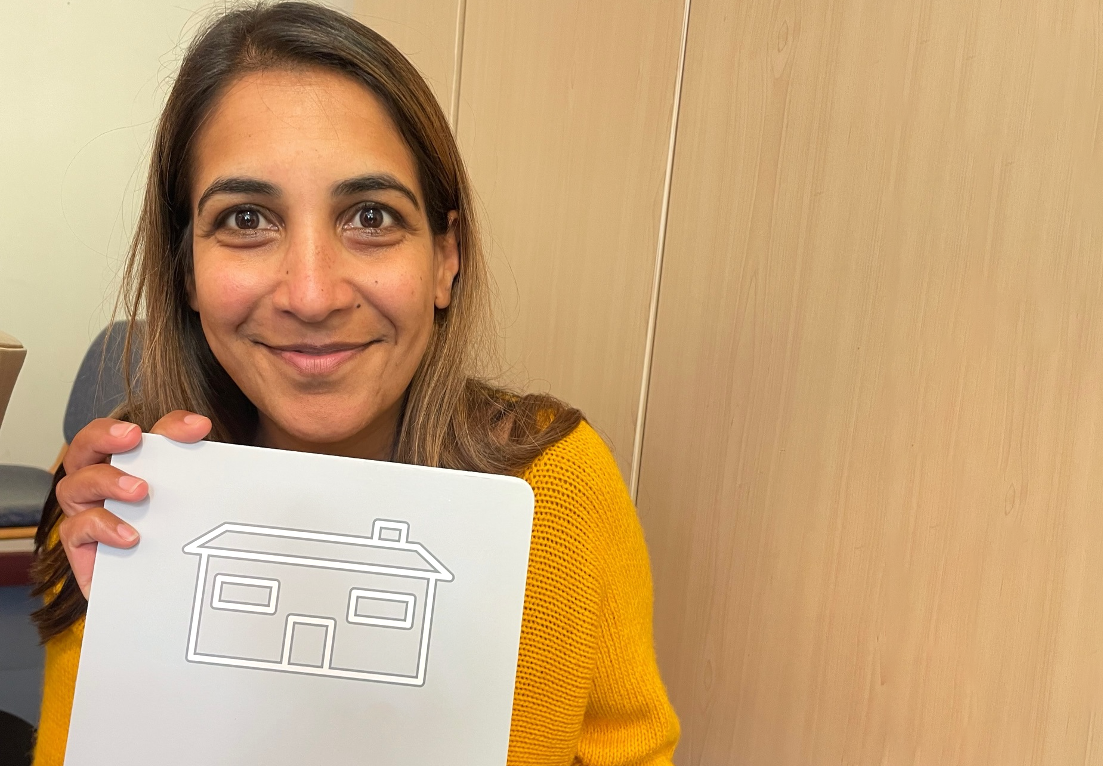 Malvi holds up a card with an image of a house on.