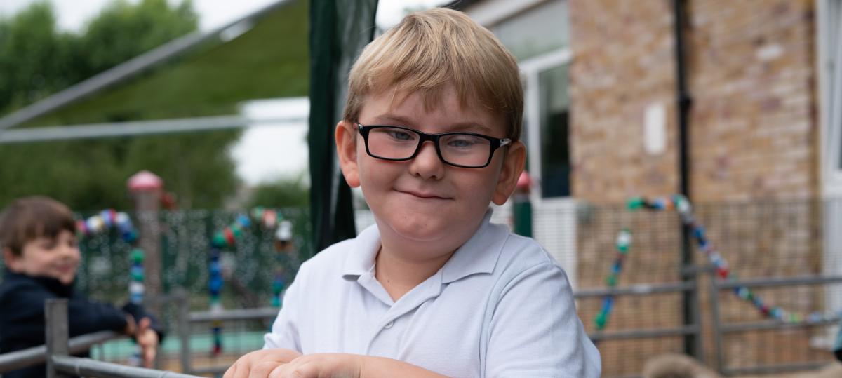 Nathan, a little boy in glasses, leans on a fence