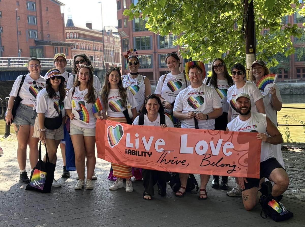 The team at Bristol pride wearing rainbow accessories and holding a SeeAbility live love thrive belong banner