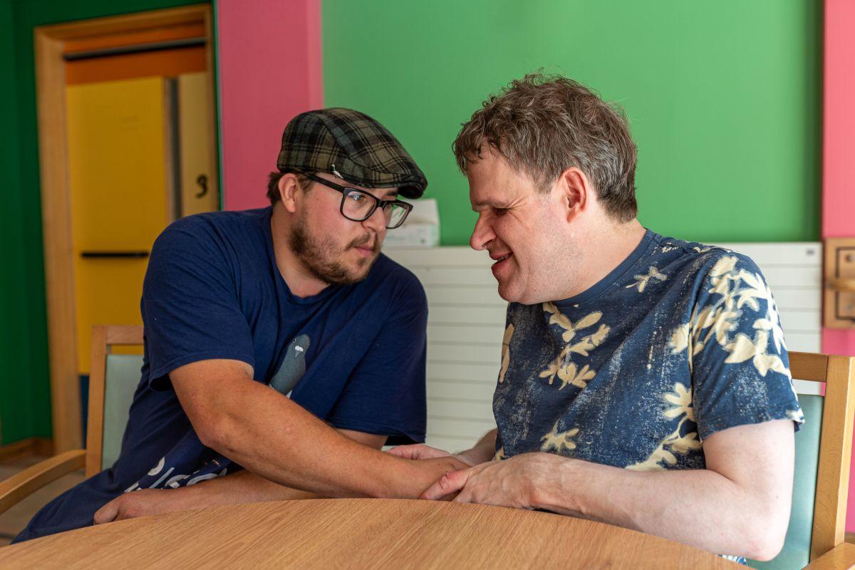 Ben and Jeremy in a coffee shop sitting close and embracing
