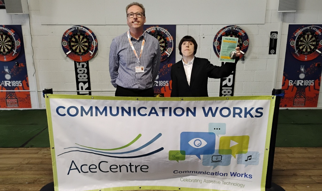 Steve and Rebecca stand behind a large banner which says 'Communication Works 2026'