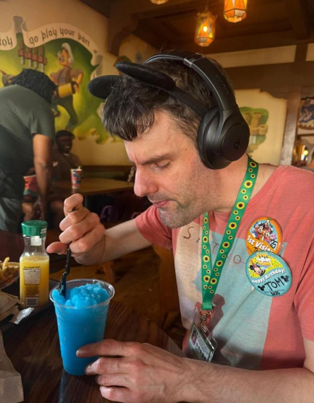 Tom at Disneyworld wearing black mickey mouse ears and drinking a blue slushy