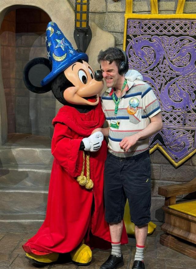 Tom at Disneyworld meeting Micky Mouse, hugging him and smiling