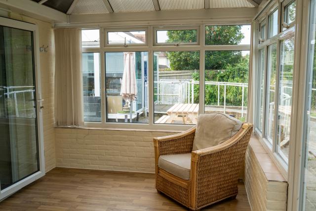 The annexe conservatory in Applewood, showing an open space with a chair, window overlooking the garden, and laminate flooring. 