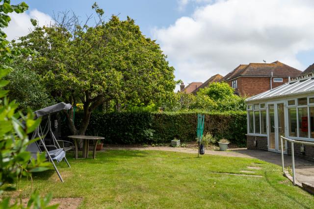 The garden at Applewood, showing a large grassy area, potted plants, a swing chair and a paved path towards the annexe. 