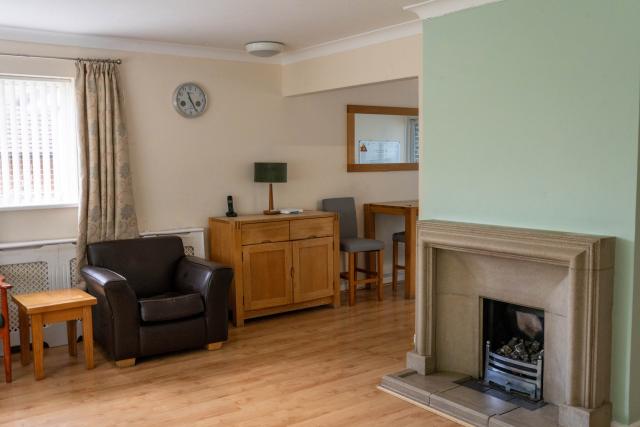 The living room at Applewood, showing a seating area with a table, fireplace, and laminate flooring.