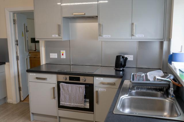 The main kitchen in Applewood, showing a large marble counter-top with labelled cabinets, a sink and a cooker.