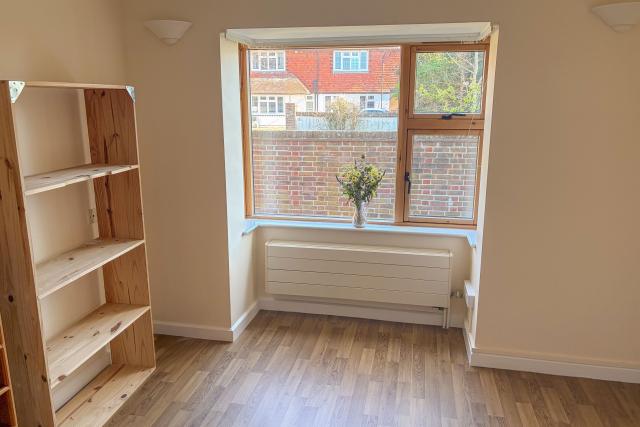 An empty bedroom in Barclay House, showing a spacious open floor space next to a bright window and wooden bookcase.