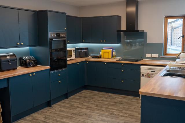 The kitchen at Barclay House, showing a modern layout filled with blue cupboards, a wooden countertop and integrated cooker. 