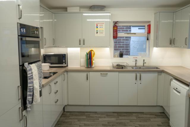 The kitchen at Denecroft, showing a spacious area with modern cabinets placed on the walls and along the ground, complete with a built-in cooker. A large kitchen counter can be seen, including a sink.