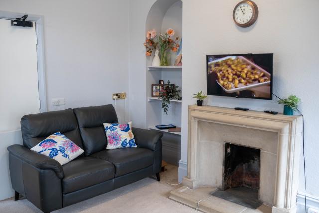 A communal living room at Denecroft, showing a sofa in front of a white wall. There's also a fireplace with a TV set above it.