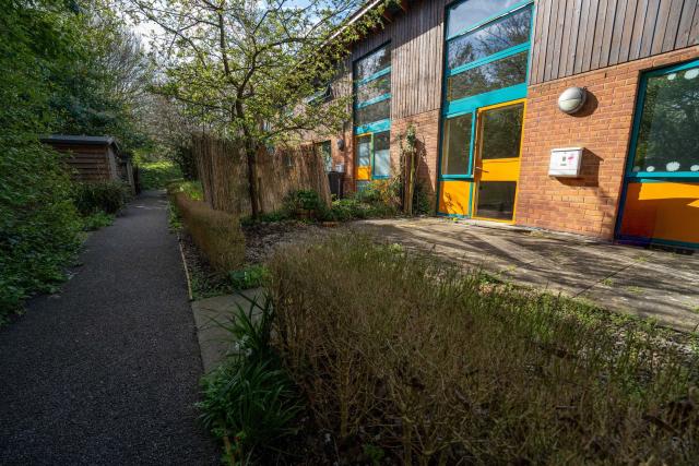 The outside of some of the flats at Honiton from the back, showing a walkway flanked by hedges and the rear of the building.