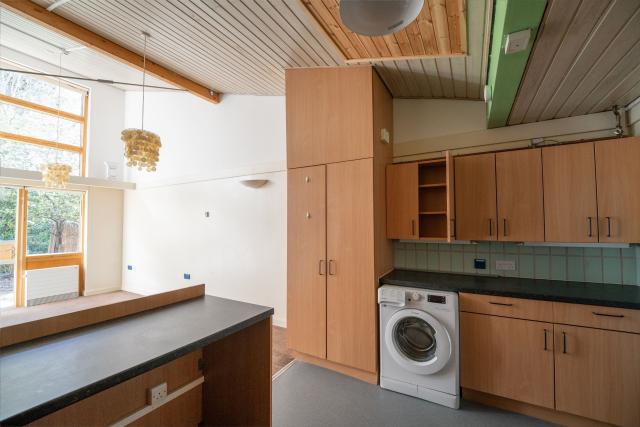 A kitchen at Honiton, showing a bright open area with kitchen surfaces, wooden cupboards, and a washing machine.
