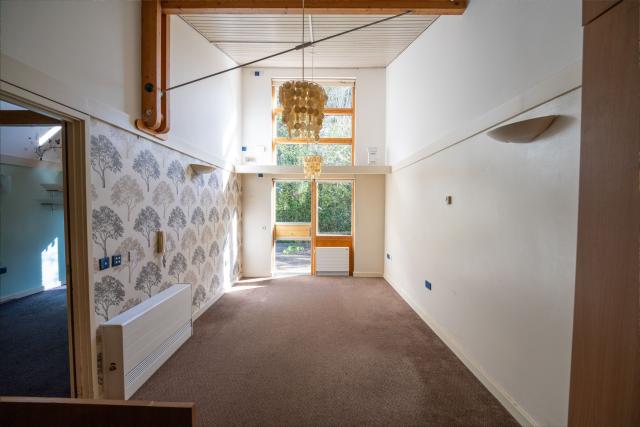 A living room in Honiton, showing a spacious open area with an opening to another room at one end and an exit to the walkway at the rear.
