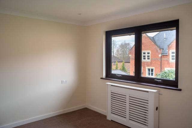 A bedroom at Spencer Court, showing brightly painted walls and a large bright window with a view to the surrounding homes.