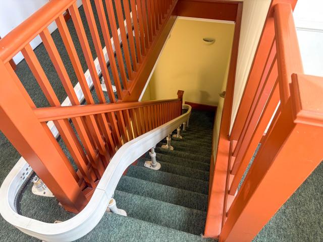 The stairlift in Surbiton, showing a carpeted staircase and the track of a stairlift snaking downwards.