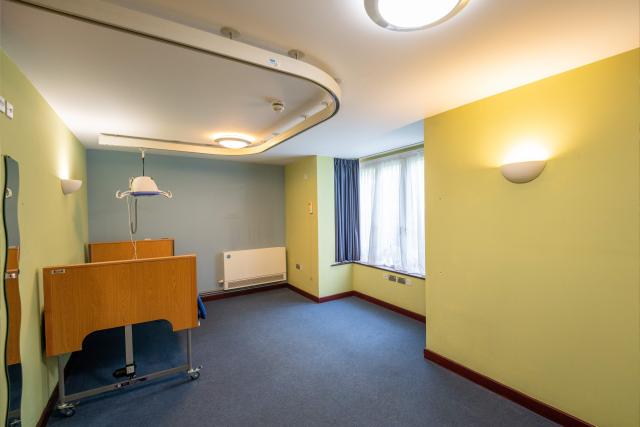 A bedroom at the Willows, showing a wide open space with yellow walls, a blue floor, and a bed with a hoisting mechanism.