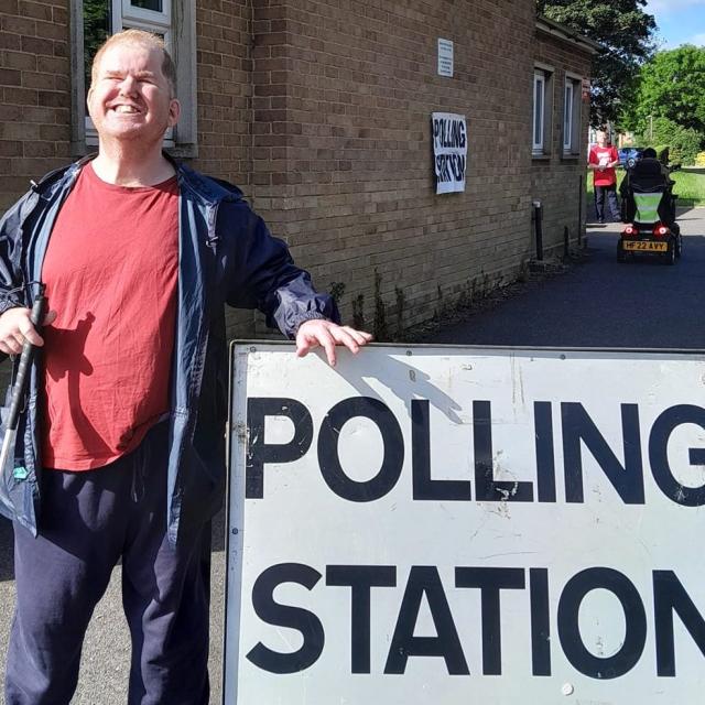 Andrew outside a polling station with his white cane