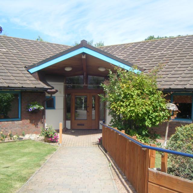The outside of Fiennes House, showing a bright gabled entrance surrounded by flowers and greenery.