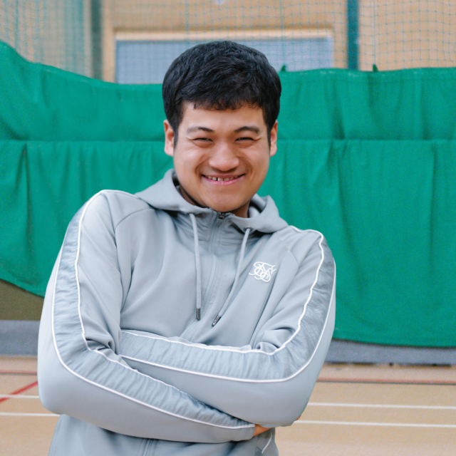 Giban smiling in a badminton court with his arms crossed