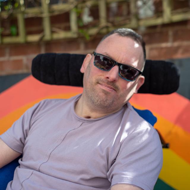 James smiling outside with a rainbow behind him