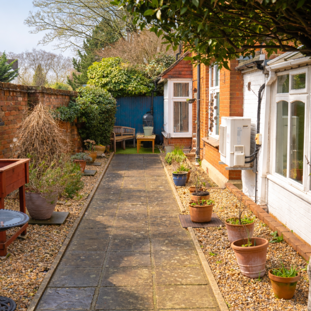 A photo of the garden and walkway behind Denecroft, showing a paved walkway lined with pebbled borders and potted plants.