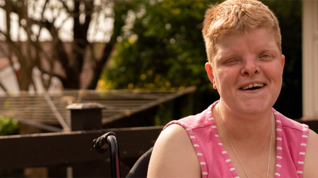 Emily smiles in her garden wearing a bright pink shirt