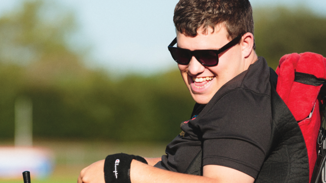 Greg beams as he drives his wheelchair around outside