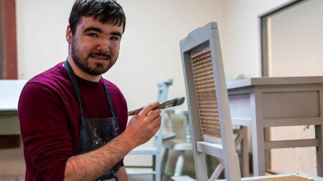Ed smiles as he paints a chair in his woodwork workshop
