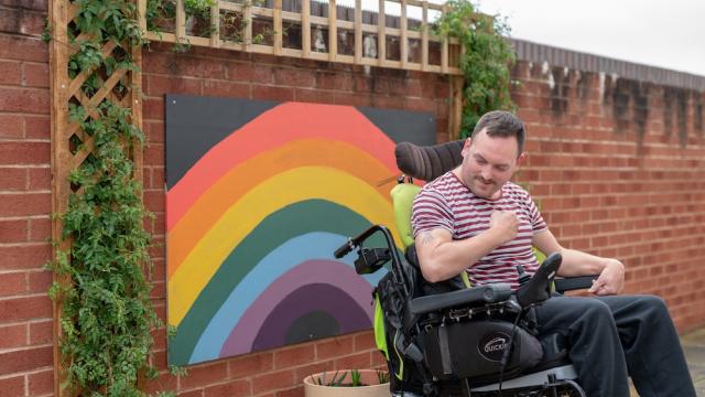 James shows off his new arm muscles in front of a painting of a rainbow