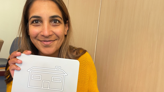 Malvi holds up a card with an image of a house on.