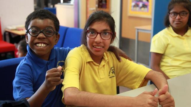 Three children wear glasses, bright school uniforms and big smiles for the camera