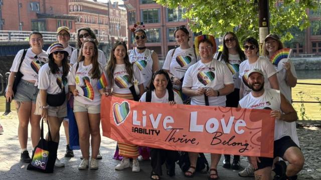 The team at Bristol pride wearing rainbow accessories and holding a SeeAbility live love thrive belong banner