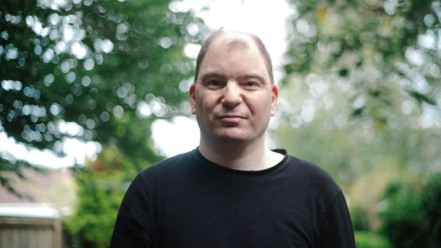 Matthew standing in a leafy area staring at the camera 